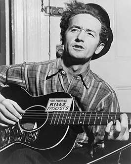 Image of Woody Guthrie playing guitar with a 'this machine kills fascists' sticker on it.